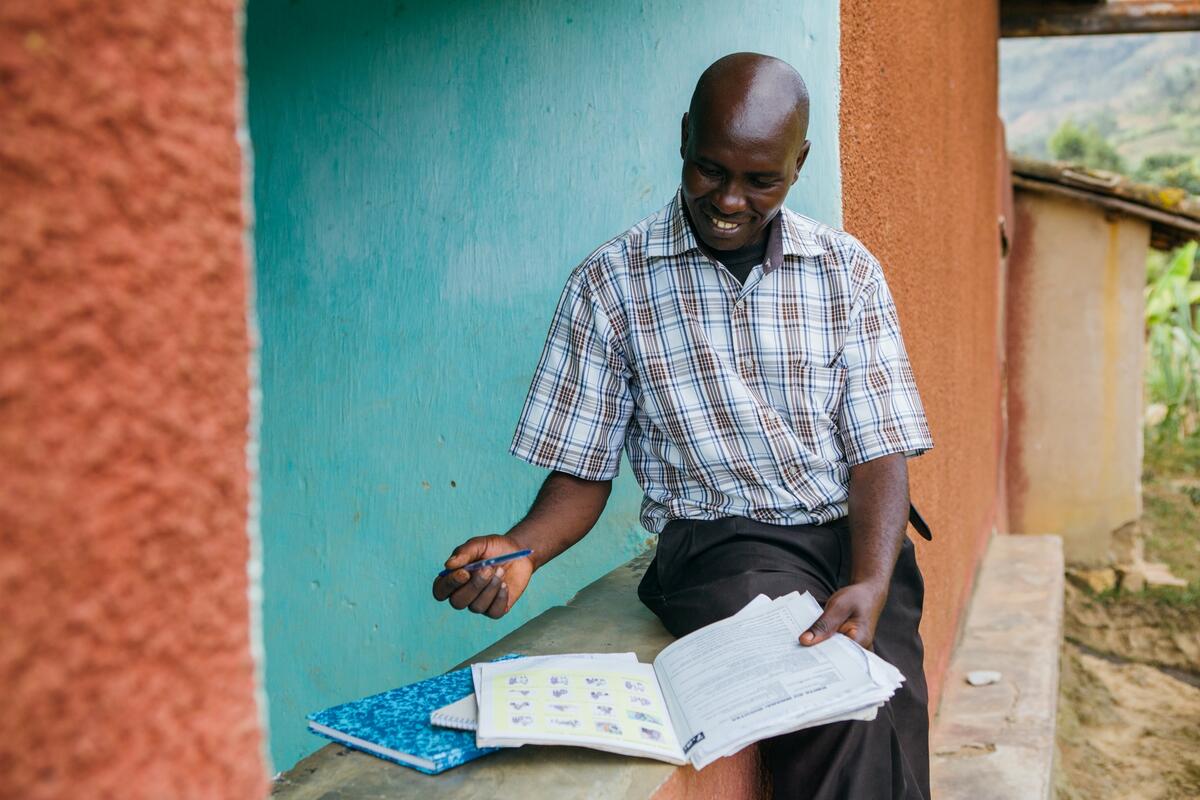 Sitting man outside consulting document in Rulindo, Rwanda,